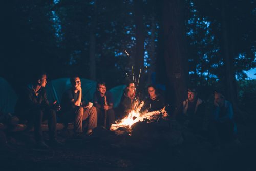 Young adults sitting around a campfire at night.